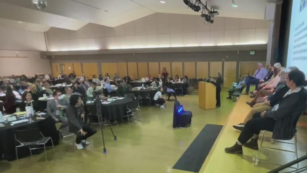 People sitting in a large room holding a recorded forum.